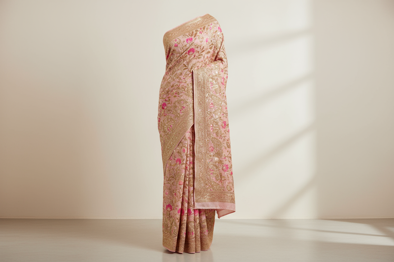 A premium embroidered saree with fine golden threadwork and shimmer, ivory or blush pink tone, luxurious minimal studio background — full-length product view, saree fully visible from top to bottom, centered composition, straight front angle, fits completely within frame height 60vh, no text, no watermark, no logo.